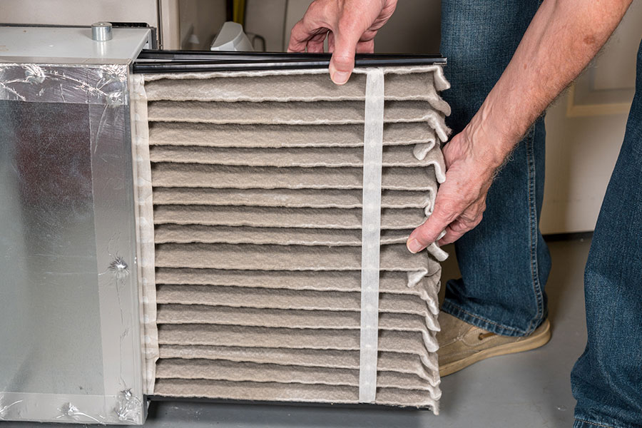 Professional HVAC technician with blue jeans pulling a dirty air filter from the furnace of a residential home in the Metro East area