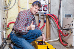 An experienced HVAC technician squatting next to a furnace with a tool and a thumbs up to indicate quality furnace inspection services in the Metro East.