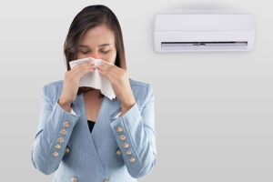 A female homeowner in Metro East Illinois, blowing her nose in front of her AC mini-split system.