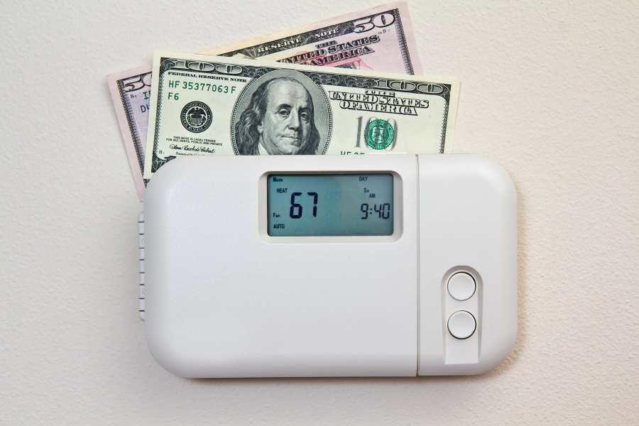 A thermostat with money on top, signifying the heating costs to keep everyone comfortable in the office in Metro East, IL.