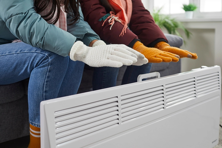 A young couple dressed in coats, scarves, and gloves warms their hands by the electric heater during the winter months in the Metro East Area of Illinois.